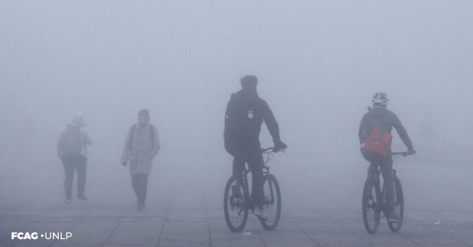 En la imagen se observan dos ciclistas que pedalean en medio de la niebla y dos personas caminando, todas bien abrigadas. En la imagen se observan dos ciclistas que pedalean en medio de la niebla y dos personas caminando, todas bien abrigadas.